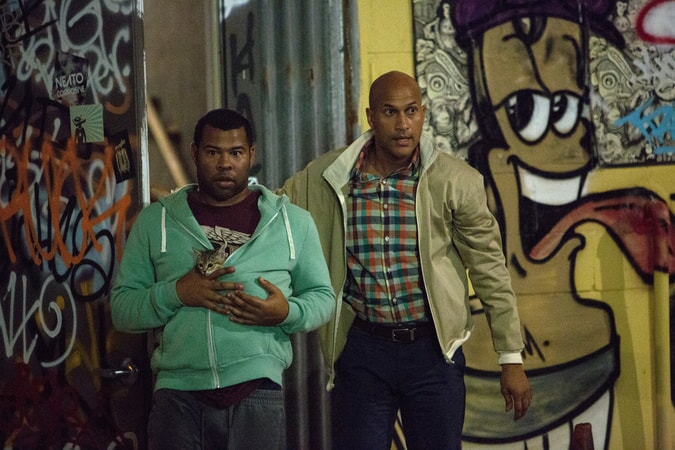 JORDAN PEELE as Rell, holding Keanu the kitten in his sweatshirt and KEEGAN-MICHAEL KEY as Clarence, walking through the street with graffiti in background