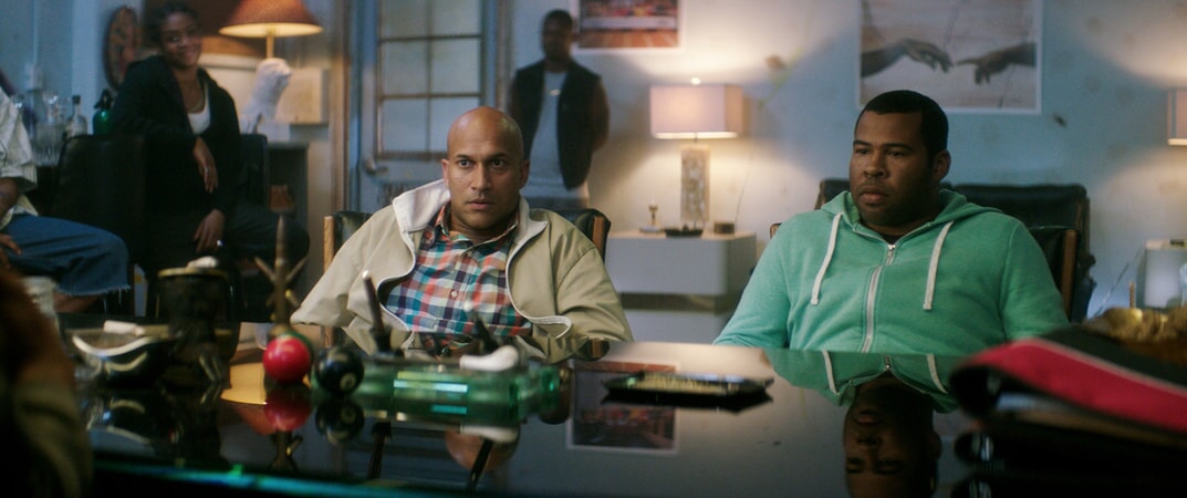 KEEGAN-MICHAEL KEY as Clarence and JORDAN PEELE as Rell sitting a desk surrounded by people